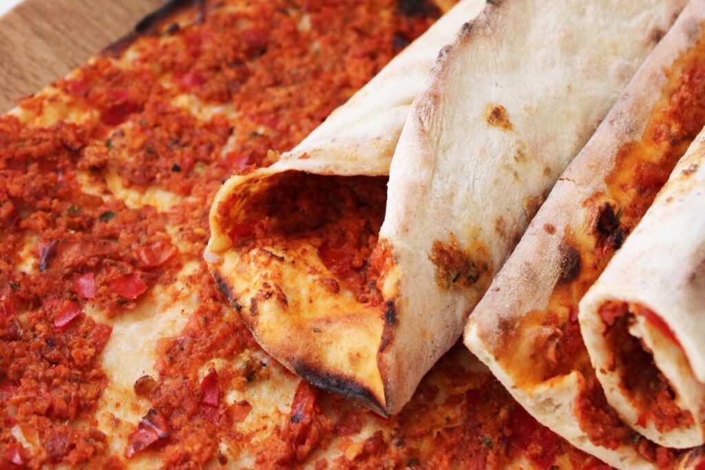 Lahmacun Döner gerollt mit Döner-Fleisch, Salat, Tomaten und Sauces auf weißem Teller, türkische Pizza gefüllt wie Döner